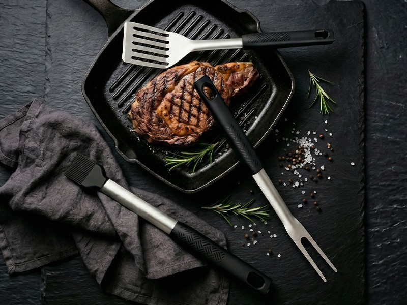 L-TOOLS cooked steak on a grill with spatula and tongs, highlighting outdoor cooking and BBQ preparation.