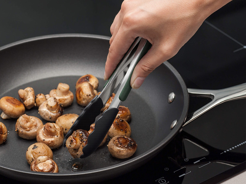 L-TOOLS hand using kitchen tongs to sauté mushrooms, demonstrating precise cooking techniques.