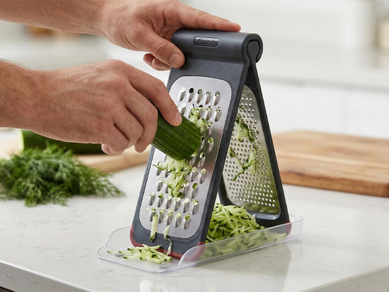 L-TOOLS multi-surface grater being used in a kitchen, emphasizing ergonomic cooking tool design.