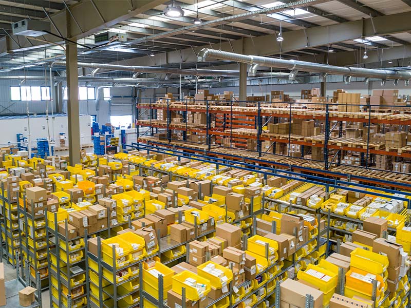 L-TOOLS busy warehouse with stacked yellow boxes and organized storage, representing logistics efficiency.