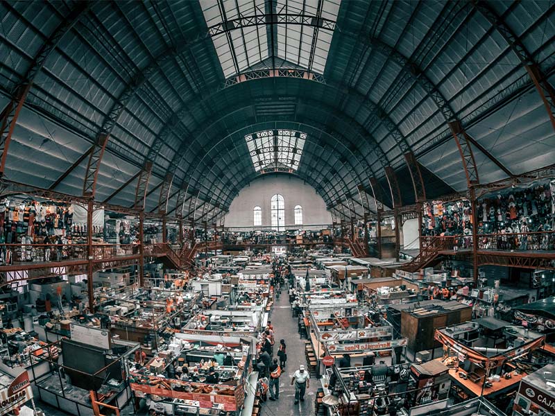 L-TOOLS aerial view of busy indoor marketplace with structured walkways and crowds, emphasizing commerce activity.