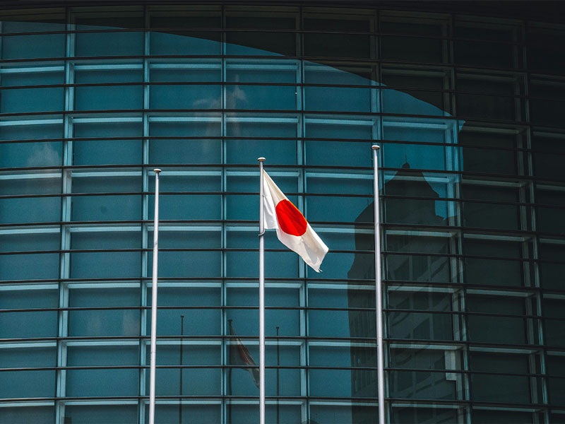 L-TOOLS Japanese flag flying in front of a modern building, highlighting national pride.