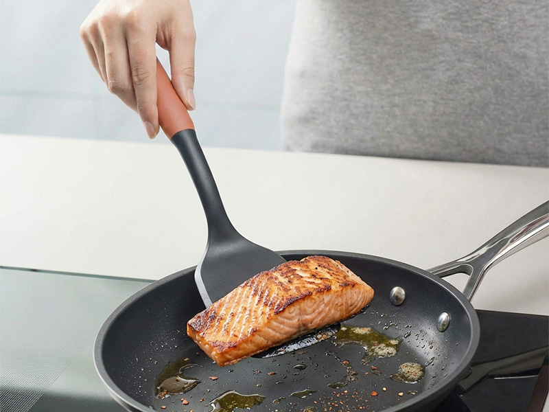 L-TOOLS hand cooking broccoli in a pan using a silicone spatula, highlighting efficient kitchen utensils.