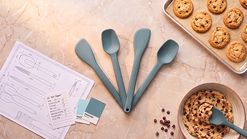 Classic spatula, spoonula, sauté spatula and scraping spoon displayed with baking tools and freshly baked cookies