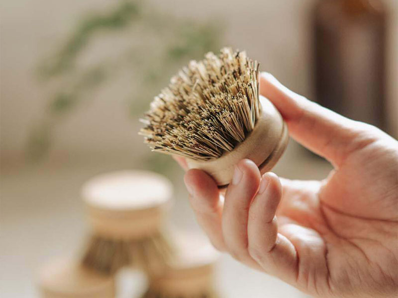 L-TOOLS person holding a round wooden brush, highlighting natural and sustainable cleaning tools.