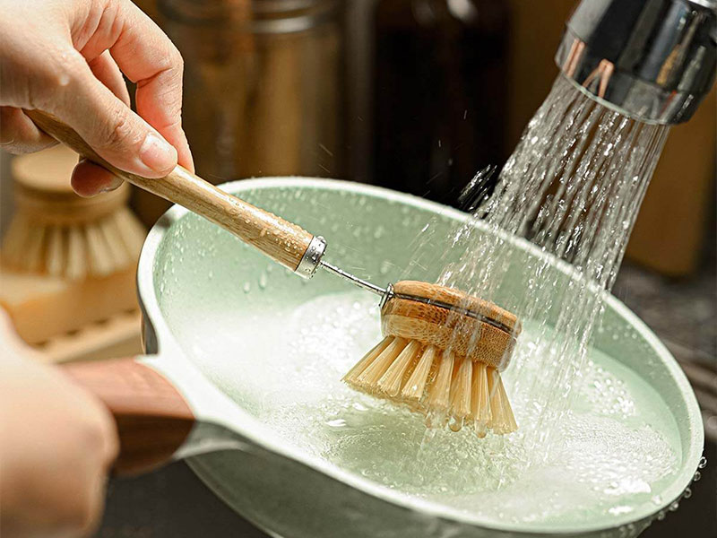 L-TOOLS scrubbing a plate with a wooden brush, emphasizing practical kitchen cleaning.