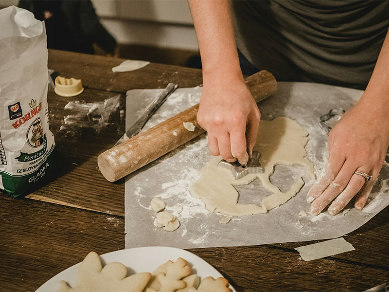 L-TOOLS person rolling dough with a rolling pin on a wooden surface, demonstrating home baking.