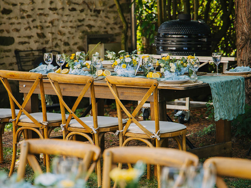 L-TOOLS close-up of wooden chairs and table setup with decorative plates and flowers for an outdoor event.