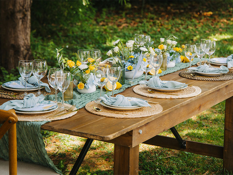 L-TOOLS rustic wooden table set in a garden with multiple place settings, emphasizing natural outdoor dining.